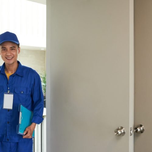 Smiling young handyman with toolbox entering home